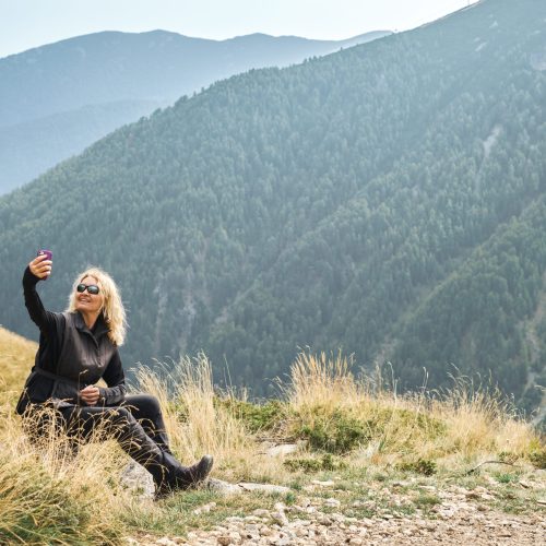 An adult woman takes a selfie at a rest stop during a hike in the mountains, active recreation.